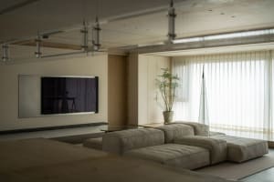 A cozy modern living room with neutral-toned fabrics, metal accents, and a large window with white curtains.