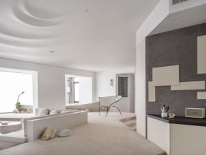 A modern minimalist living room with concrete flooring and walls, featuring a white couch, a white chair, and a concrete wall