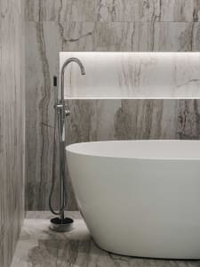 Modern minimalist bathroom with a free-standing white bathtub and marble walls and floor.
