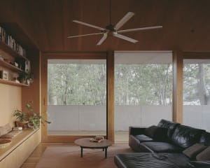 A modern living room featuring wooden walls and furniture, with large windows overlooking a forested area.