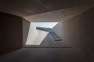 Modern interior space with concrete walls, stairs leading down to a lightwell, and a view of the outdoors.