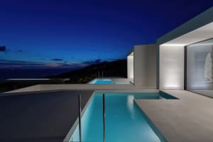 Modern villa with a concrete swimming pool at dusk, overlooking the sea.
