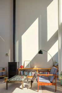 A modern living room with a glass coffee table, wooden armchair, bookshelf, and floor lamp.