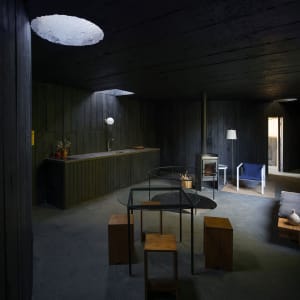 A minimalist kitchen with a concrete floor, walls, and table, and wooden stools.