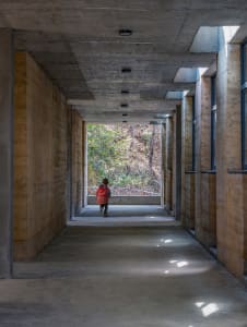 A child wearing a red jacket walks through a concrete corridor