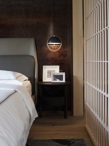 A minimalist bedroom featuring dark wood elements and a white bed with a gray headboard.