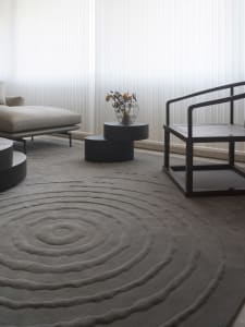 A minimalistic living room featuring a textured tiled rug, a white sofa, a black wooden armchair, and a side table with dried