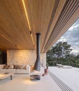 Modern living room with white couch, stone wall, wooden ceiling, and outdoor patio