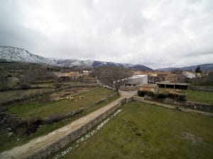 A view of a village in winter with snow-covered mountains in the background.