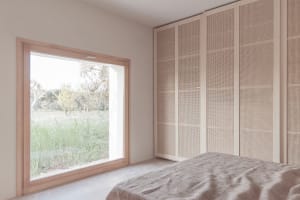 A bedroom with wooden walls and a large window overlooking a grassy field.