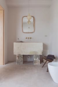 A minimalist bathroom with a concrete floating sink, white bathtub, and wooden stool with towels.