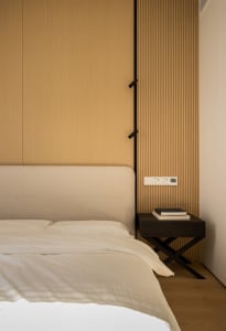A minimalist bedroom featuring a bed with a fabric headboard and a nightstand with books and reading materials.