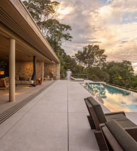 A modern residential outdoor patio featuring concrete, wood, stone, and glass elements.
