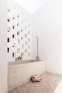 A minimalist industrial-style bathroom with concrete walls and floors, featuring a walk-in shower and a rock-like object on t