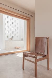 A minimalist interior with concrete walls, wooden floor, and a leather chair.