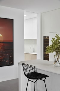 A modern minimalist kitchen with a white concrete countertop and white cabinets.