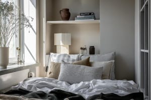 A minimalist bedroom with a bed featuring a mix of white and gray linens and decorative pillows, alongside ceramics and a del