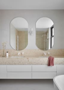 A modern bathroom featuring a terrazzo countertop with a double sink, white cabinets, and a freestanding tub in front of larg