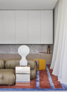 A modern living room featuring a taupe leather couch, silver coffee table, and white floor lamp.