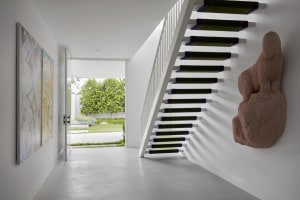 A modern staircase with metal railings and green carpeted steps leading up to a white wall with a large, abstract sculpture m