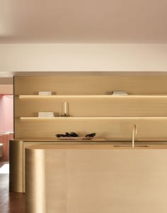 A view of a modern metallic kitchen counter with a brass faucet and a wooden backsplash.