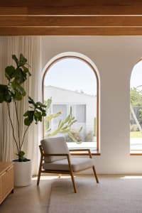 A minimalist living room with a concrete floor and arched windows, featuring a comfortable armchair and a large potted plant.