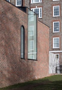 Modern brick exterior of a building with large glass window and arched glass window on stairs.