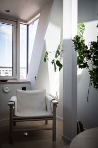 A modern interior featuring a white upholstered chair with wooden arms and legs, positioned near a window.