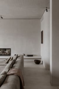 A minimalist living room with a concrete floor, a large grey sofa, and a built-in entertainment unit with a television and a 