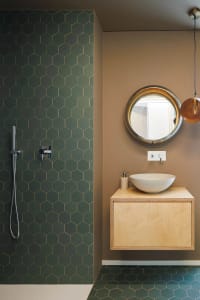 A modern bathroom features green hexagonal tiles on the walls and floor, with a floating wooden vanity and a round mirror abo