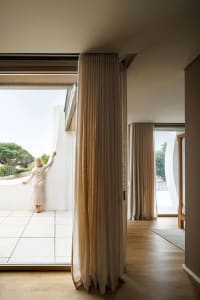 A modern living room with textured curtains and a balcony overlooking greenery.