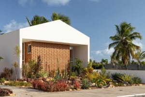 Modern building exterior with white overhang and red brick wall surrounded by colorful plants