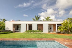 A modern house with a brick and concrete exterior, featuring a pool and outdoor seating area surrounded by greenery.