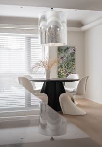 A minimalist dining room featuring a black round table and white modern chairs, surrounded by floral decor and modern lightin