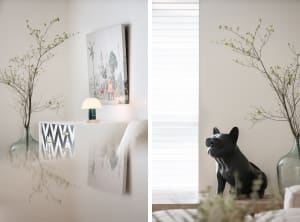 A modern living room featuring a plant with long branches in a vase, a table lamp, and a wall painting.