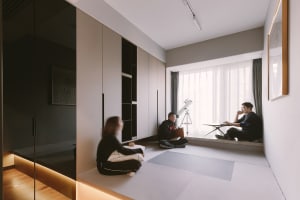 People sitting in a modern living room with concrete walls, glass windows, and wooden floors.