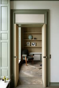 A minimalist office space with a wooden parquet floor, shelving, and a comfortable chair.