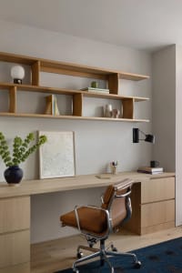 A modern office space featuring a wooden desk with shelves, a brown leather office chair, and various office supplies.