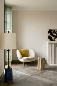 A cozy living room with a white armchair and mustard yellow pillow, featuring a wooden floor and a door in pastel green.