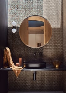 Modern bathroom with a circular mirror, sink, and mosaic tile walls.