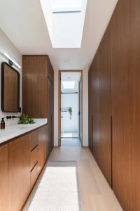 Modern bathroom with wooden cabinets, white flooring, and a skylight above a long corridor leading to a shower stall.