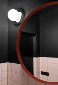 A modern bathroom with a large round mirror, black walls, and pink and white tiled floors.