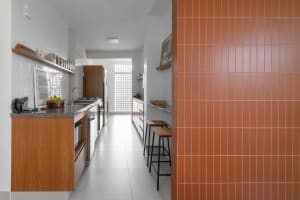 Modern minimalist kitchen with white and wood finishes and terracotta tile backsplash.