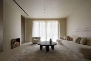 A modern minimalist living room featuring a neutral tone color palette with a curved sofa, round coffee table, and white drap