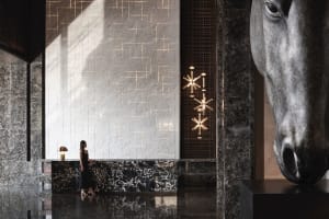 A woman standing in a luxurious industrial-style lobby with marble finishes.