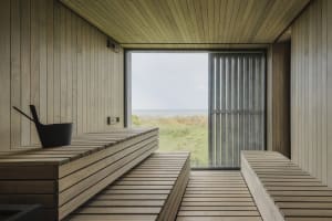 Modern industrial-style sauna with wooden benches and a large window overlooking a grassy field.