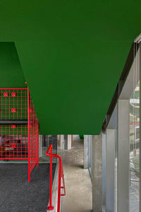 A modern corridor featuring metallic red railings and a green ceiling.