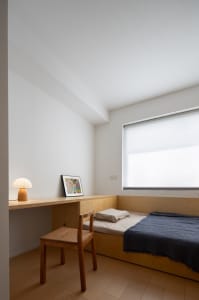 Modern minimalist bedroom with a solid wood bed, desk, and chair, featuring a large window with blinds.