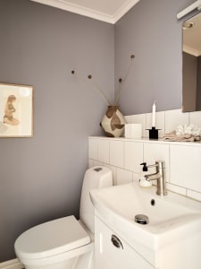 A minimalist grey bathroom interior with white ceramic tiles, a white toilet, and a white sink with a vase on the countertop.
