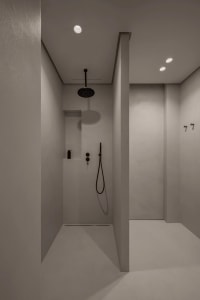 A modern bathroom with concrete walls and ceiling, featuring a black shower head and minimalist design.